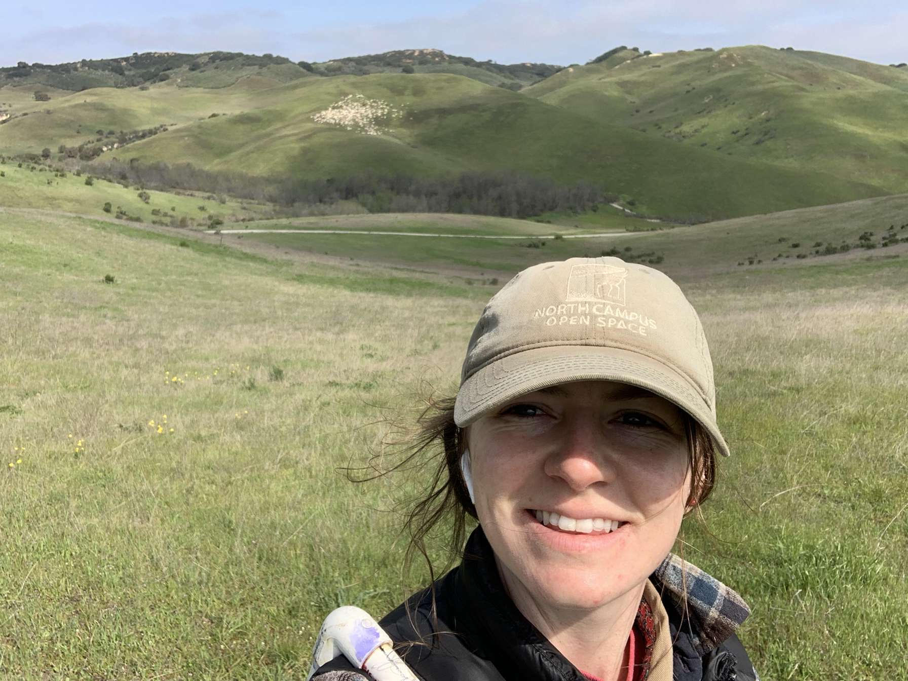 Sarah smiling and taking a selfie while standing in a grassland