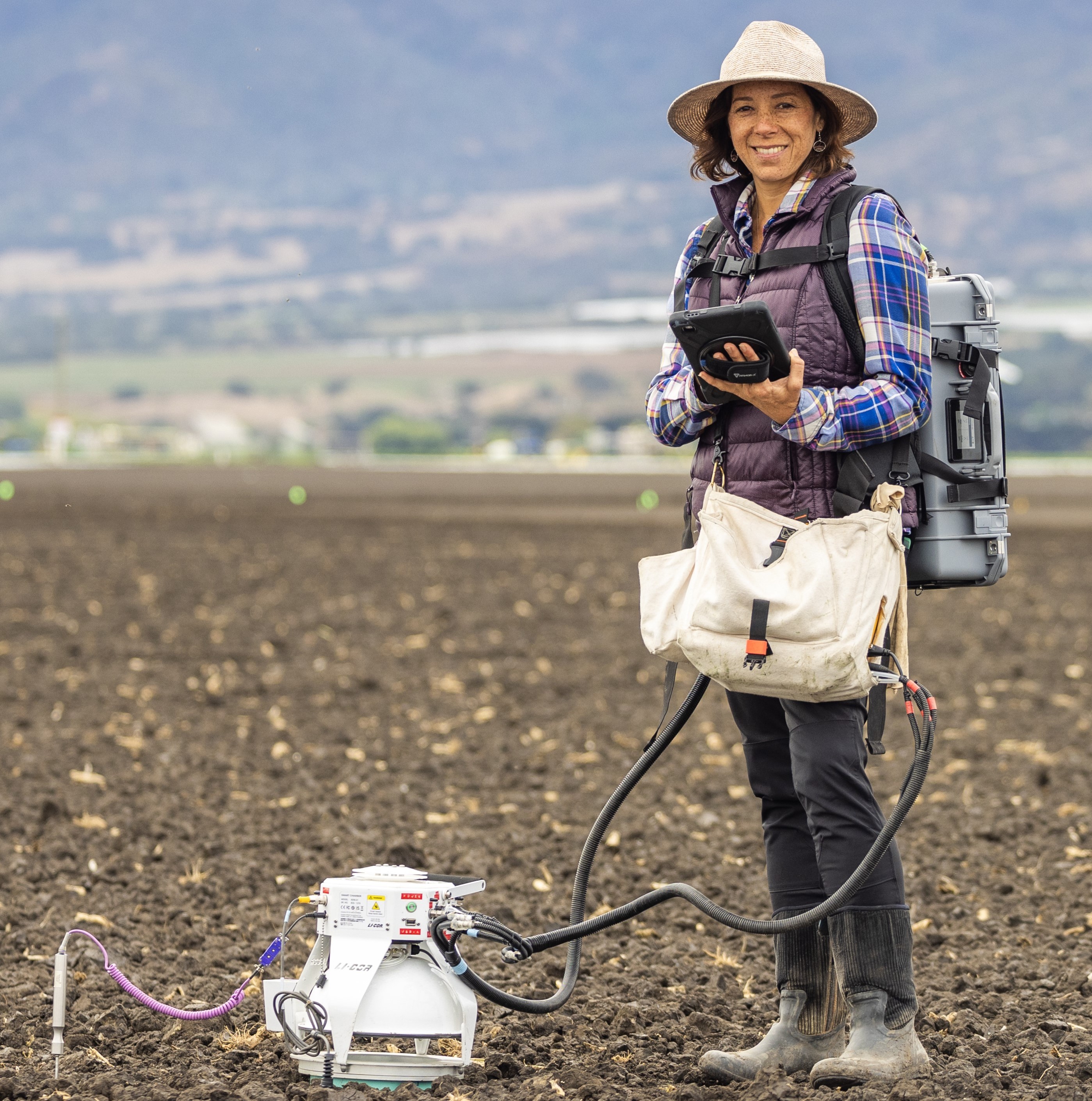 Person in a field with agricultural equipment and a tablet device.