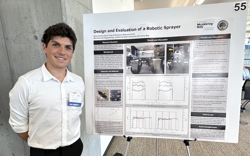 male college student smiling standing next to research poster about robotic sprayers