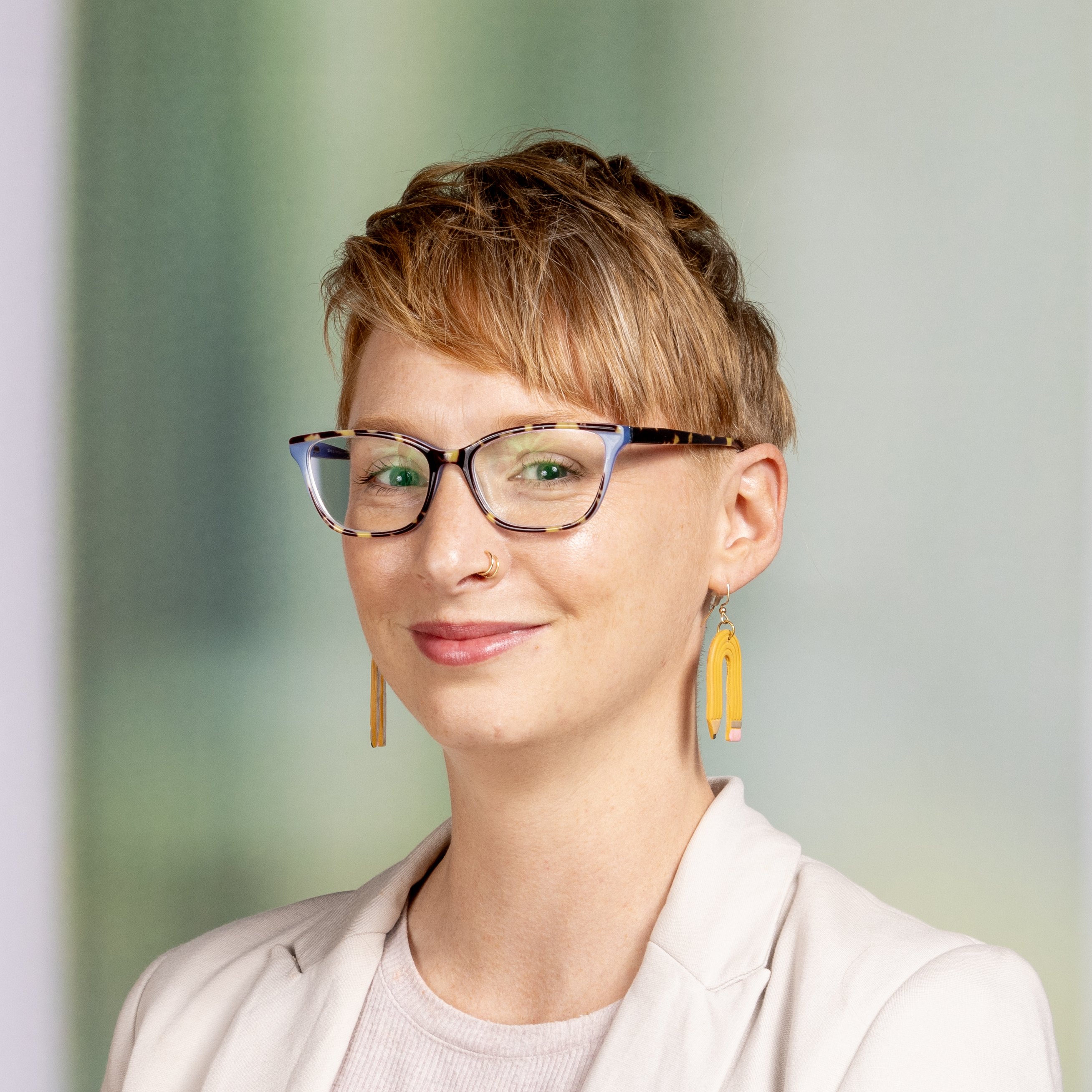 Woman with glasses and pencil earrings smiling at the camera