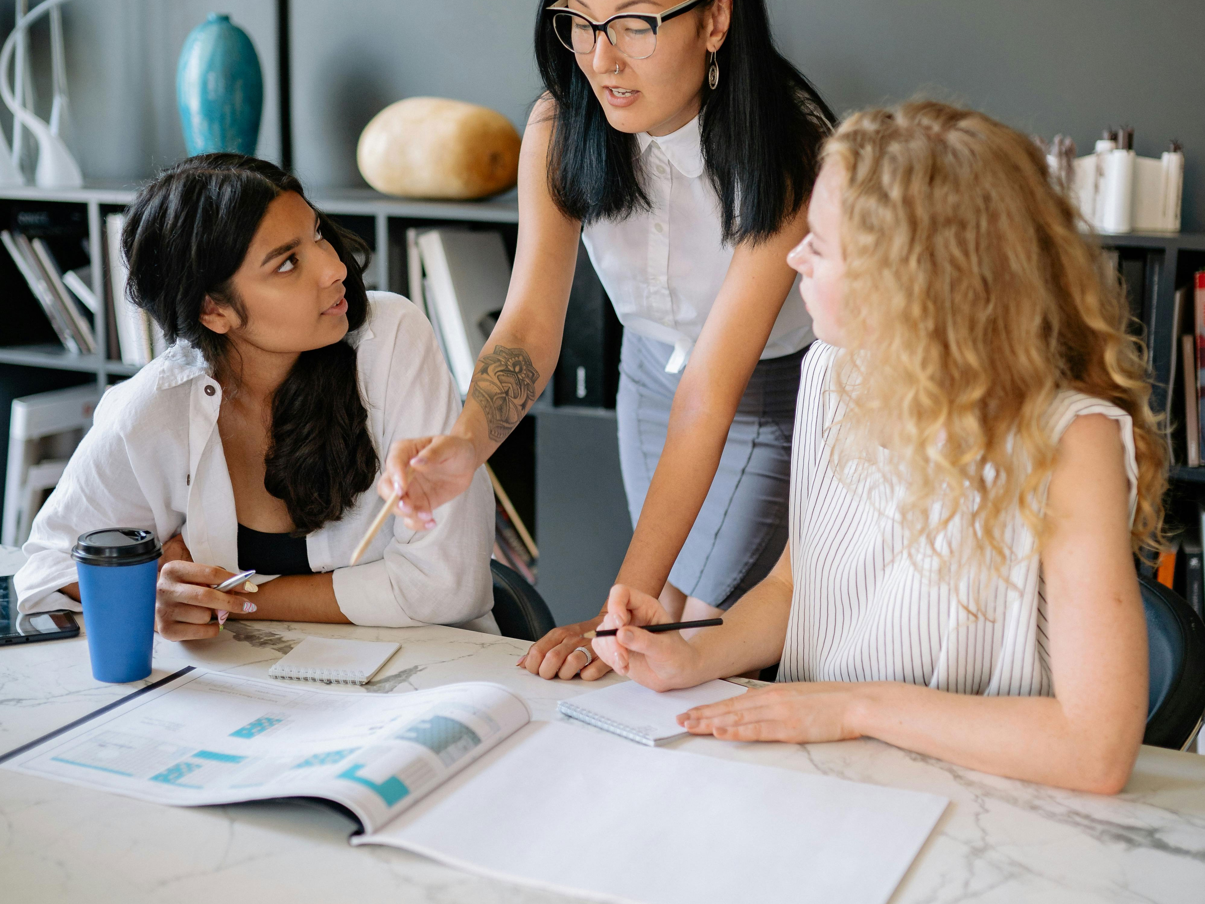 Three women at work talking at a table with documents spread out