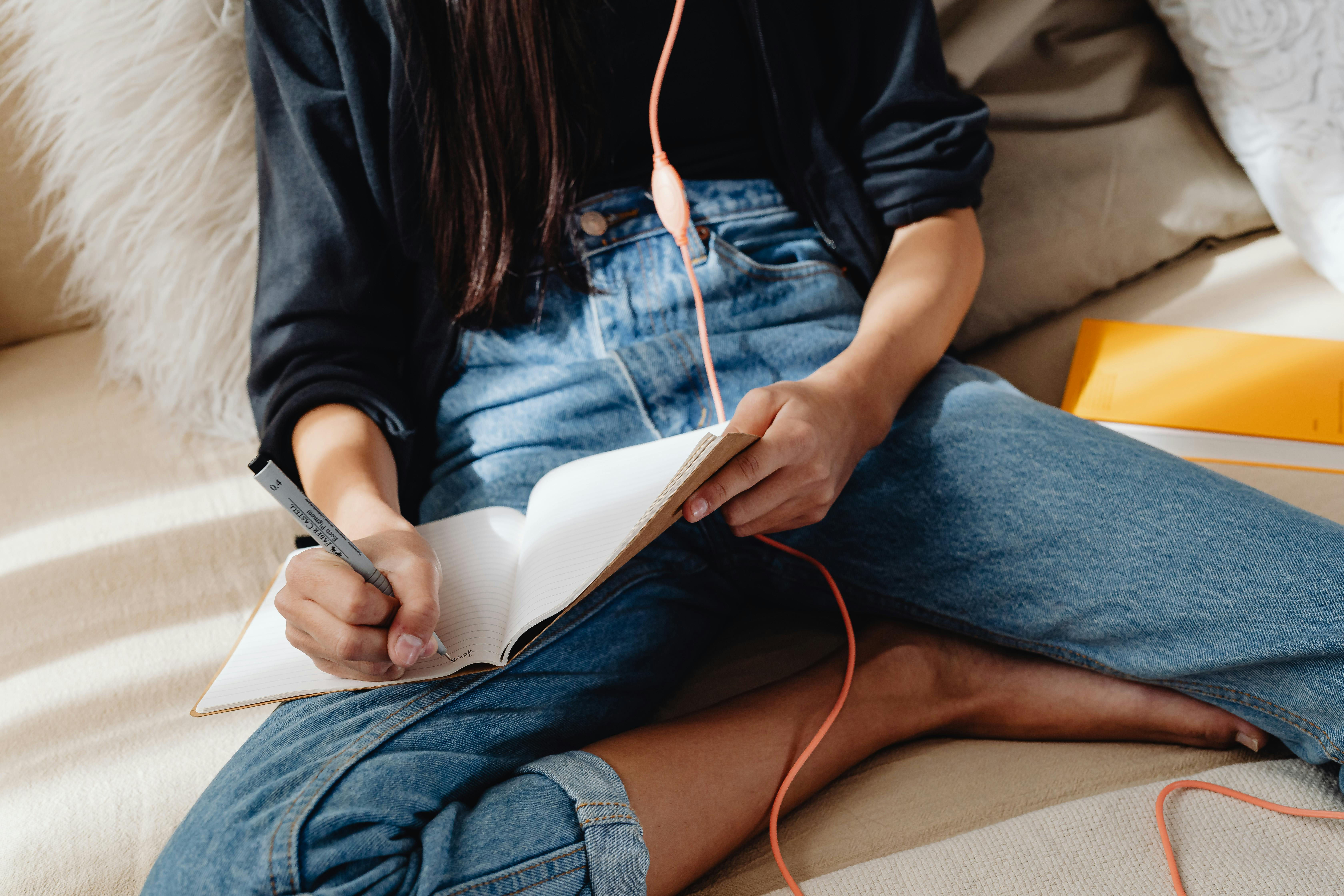 A person writing in a notebook while wearing headphones