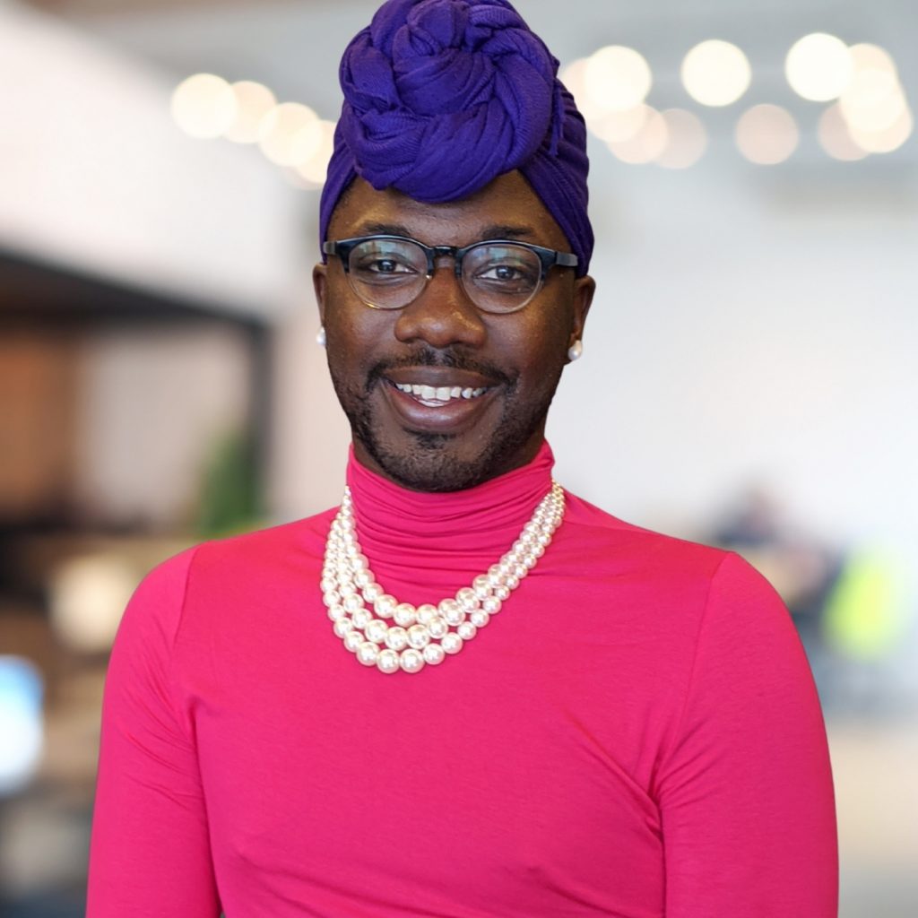 Headshot of Romeo E. Jackson with pink turtleneck, pearl necklace, and purple head wrap