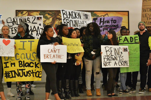 A demonstration in the CSUMB Library to bring awareness to campus about police brutality and to be in solidarity with the organizers in Ferguson, MO who were protesting the murder of Mike Brown and the police killing of multiple Latine men in Salinas, CA. A crowd of people standing in silence with signs that say “I can’t breathe” and Black-N-Brown Lives Matter.
