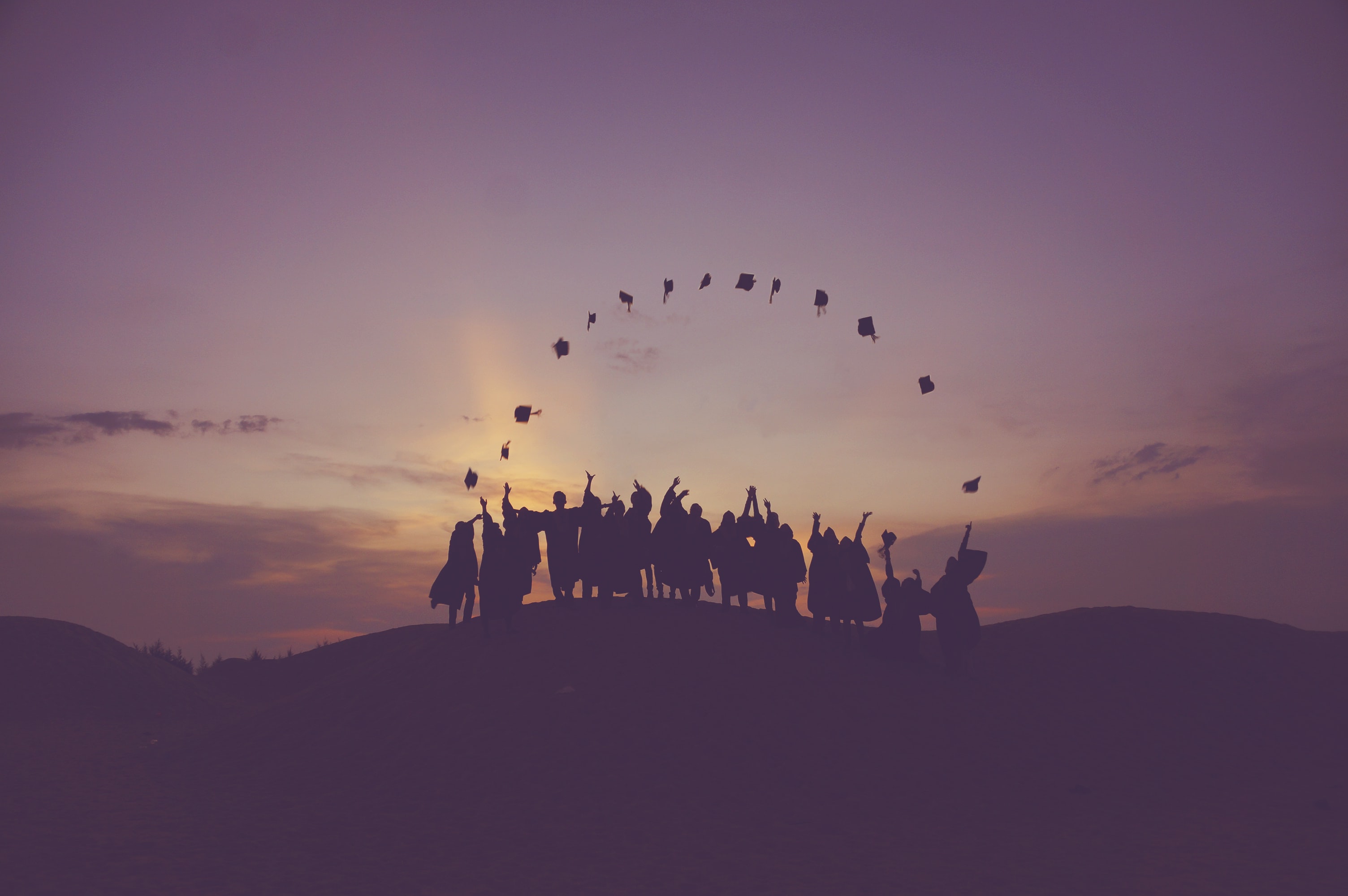 Graduating class of students in a hill over the sunset.