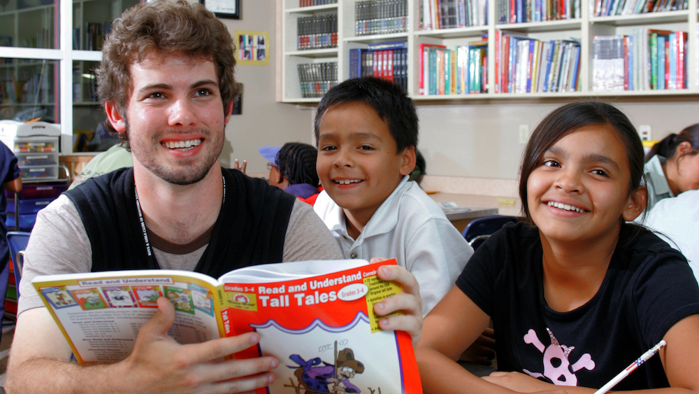 A student reading a story book to two children