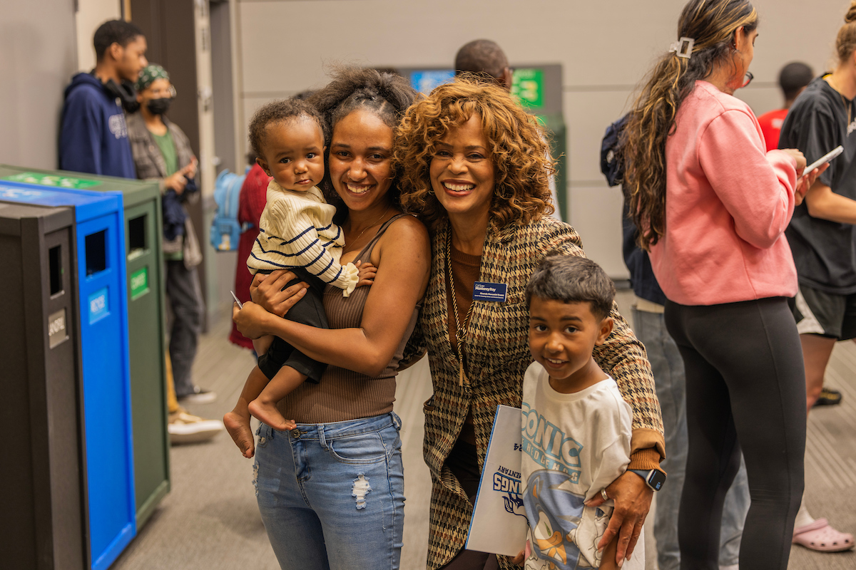 two women smiling. One is holding a small child and the other has there arm wrapped around an older child.