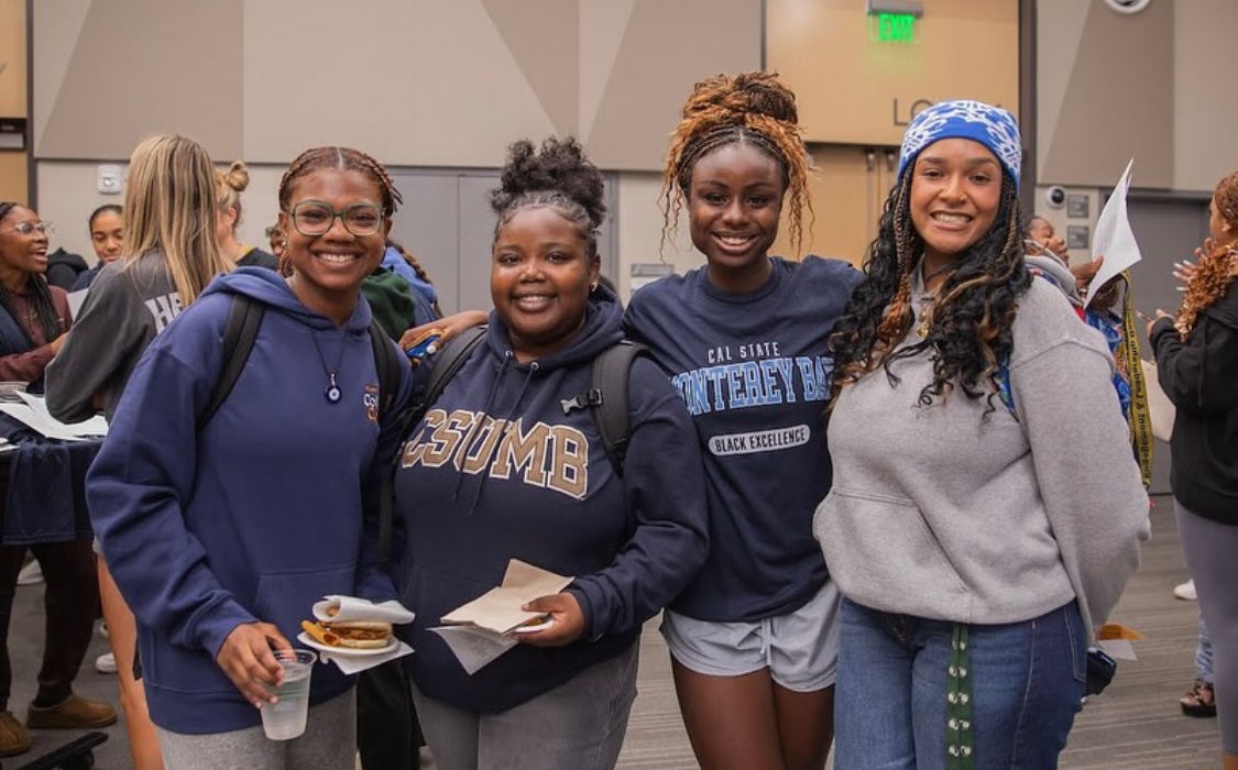 Four smiling students wearing CSUMB sweaters