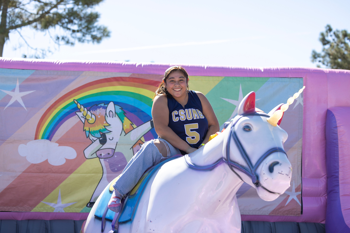 A csumb student smiling at the camera while riding a unicorn.