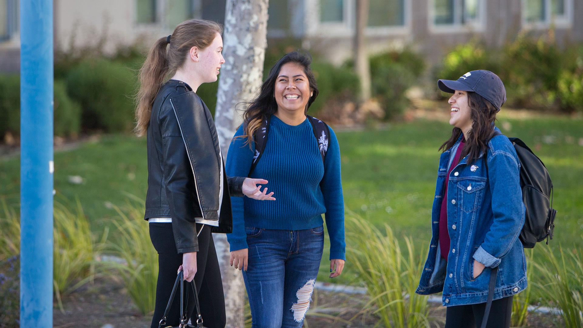 Three students talking and smiling outside.