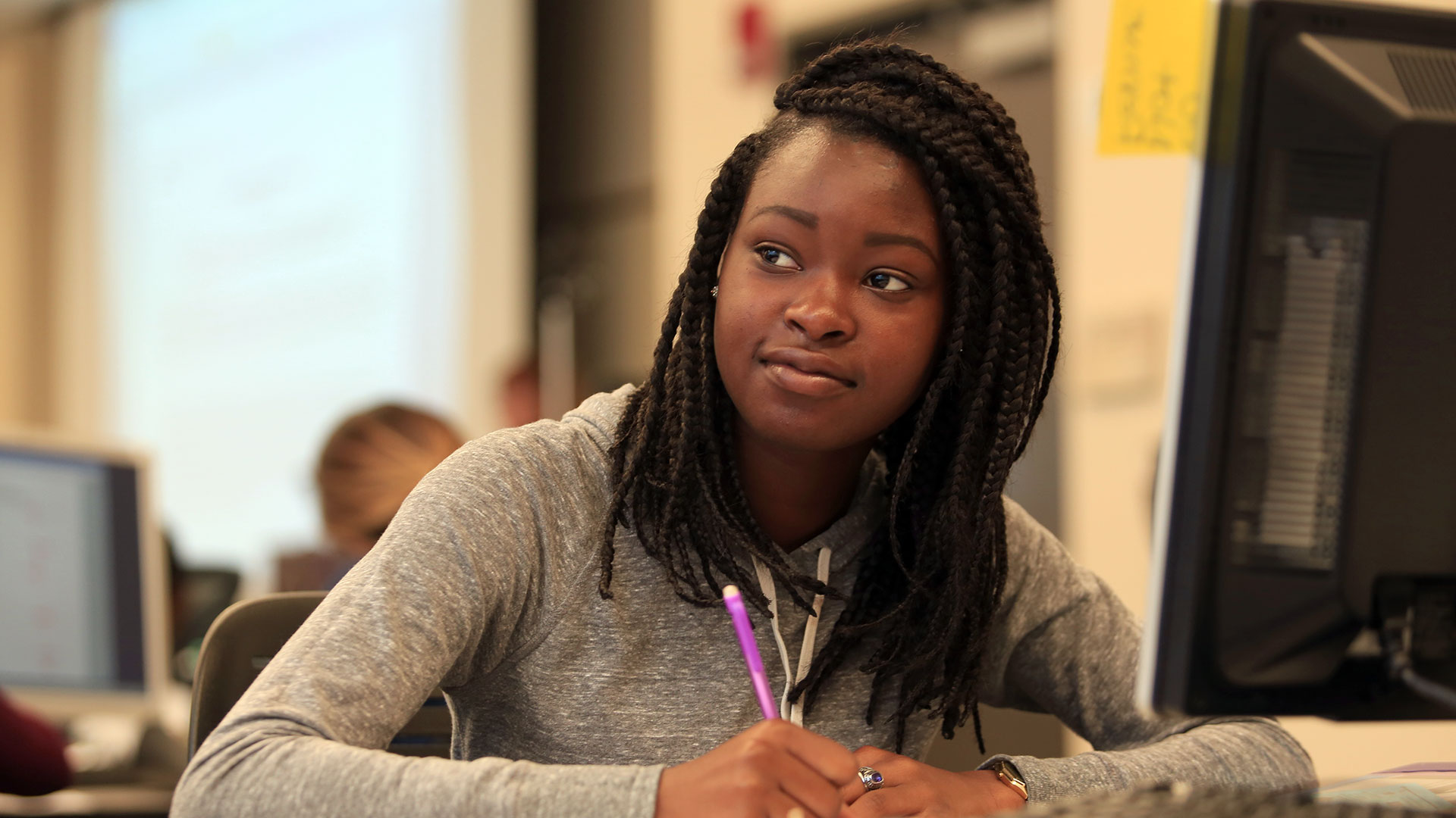 Student taking notes in class and looking off screen at someone.