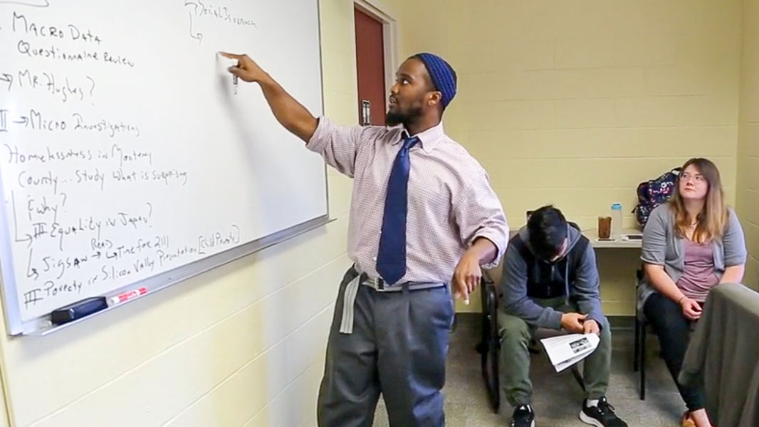Photo: Professor of liberal studies Ibrahim Shelton pointing to a whiteboard in a classroom