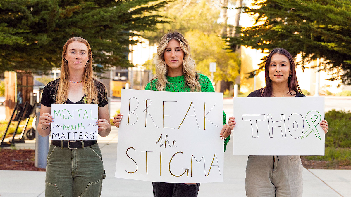 Three student-athletes holding signs in support of mental health advocacy group