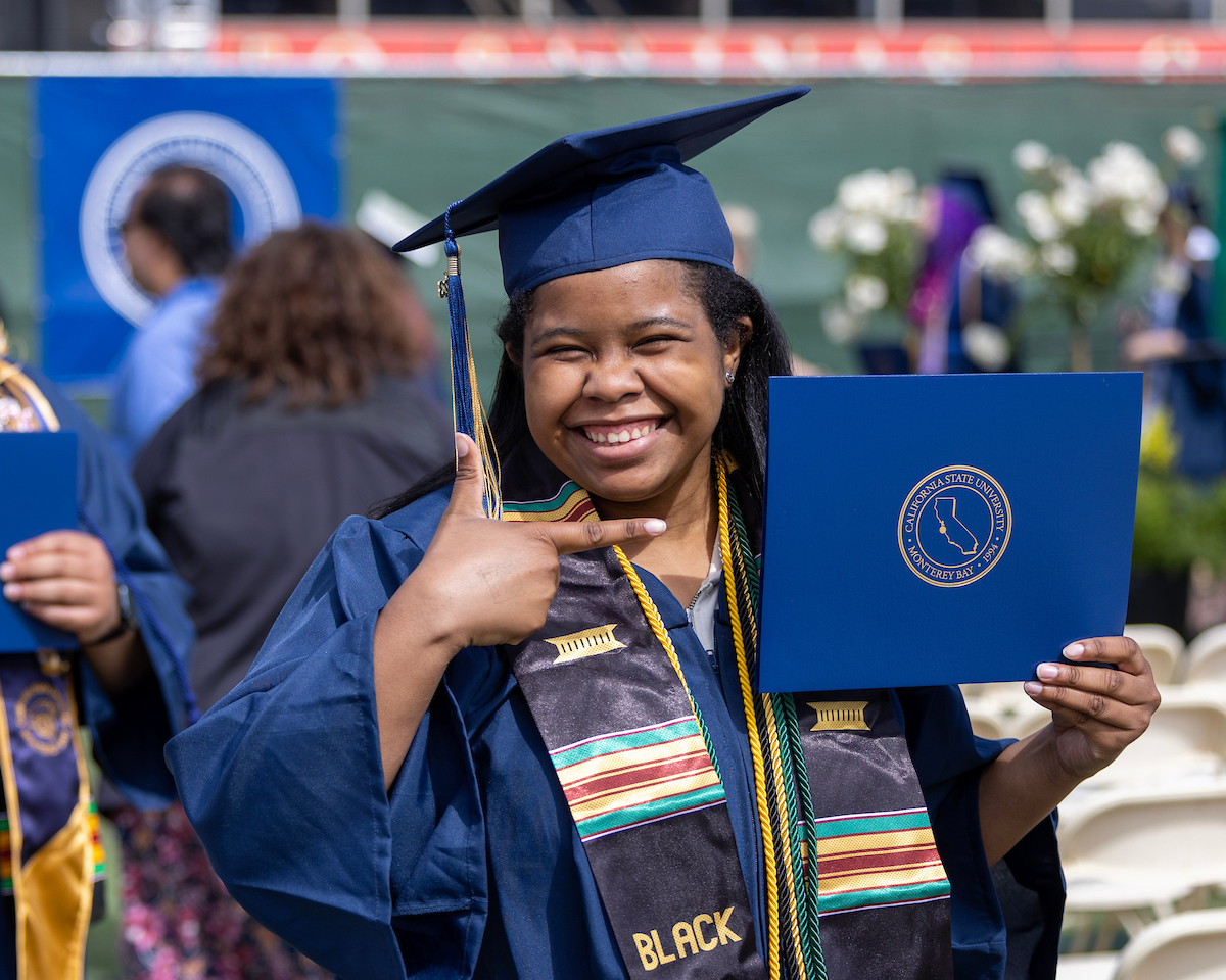 Student pointing to her diploma after the COS and COE Convocation.